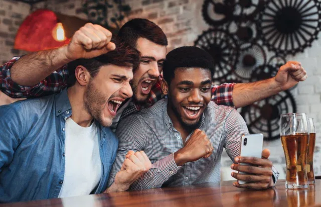 Three adults looking at a smartphone at a table in the illustrative image supplied with the Game On Ontario announcement.