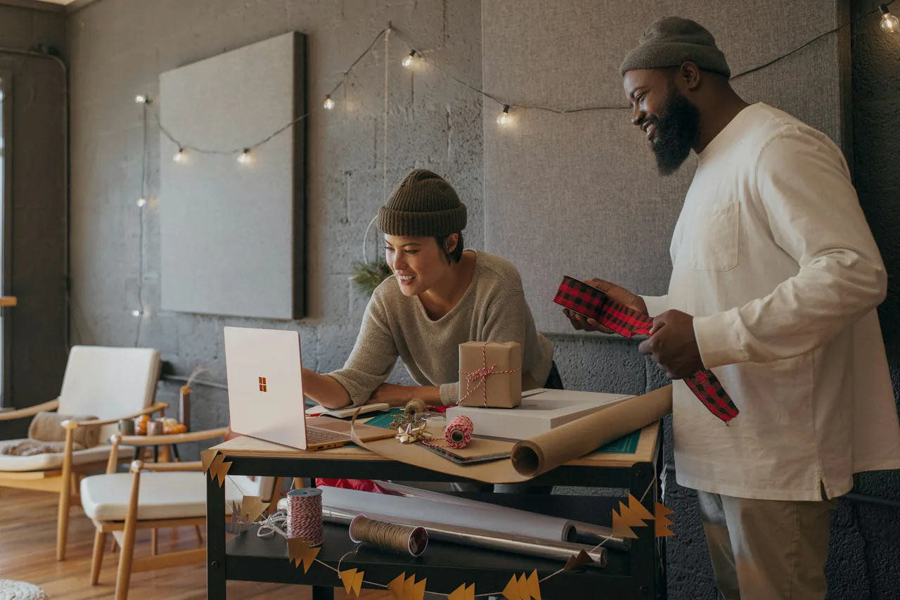 Two colleagues wrapping gifts beside a laptop