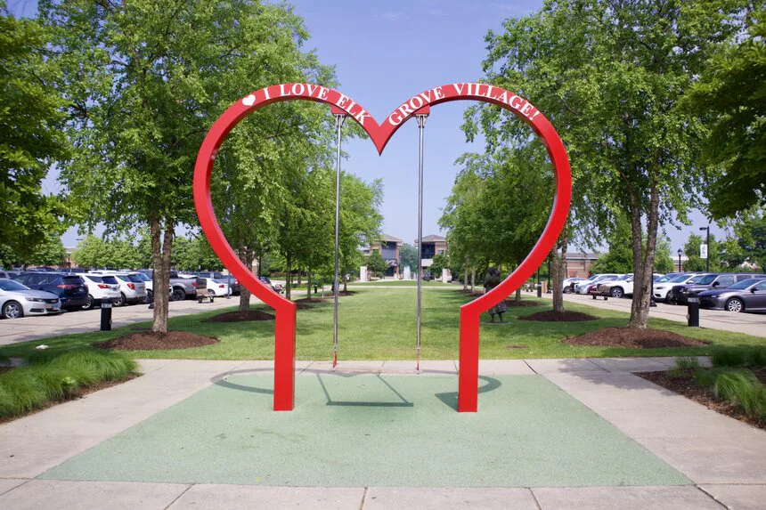 Red heart-shaped I Love My Elk Grove Village swing between trees