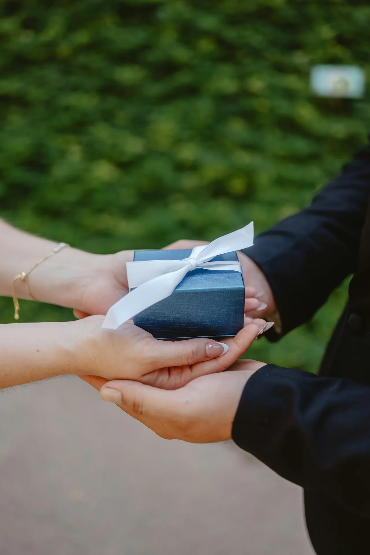 Hands passing a small blue gift box outdoors, illustrating employee gifts