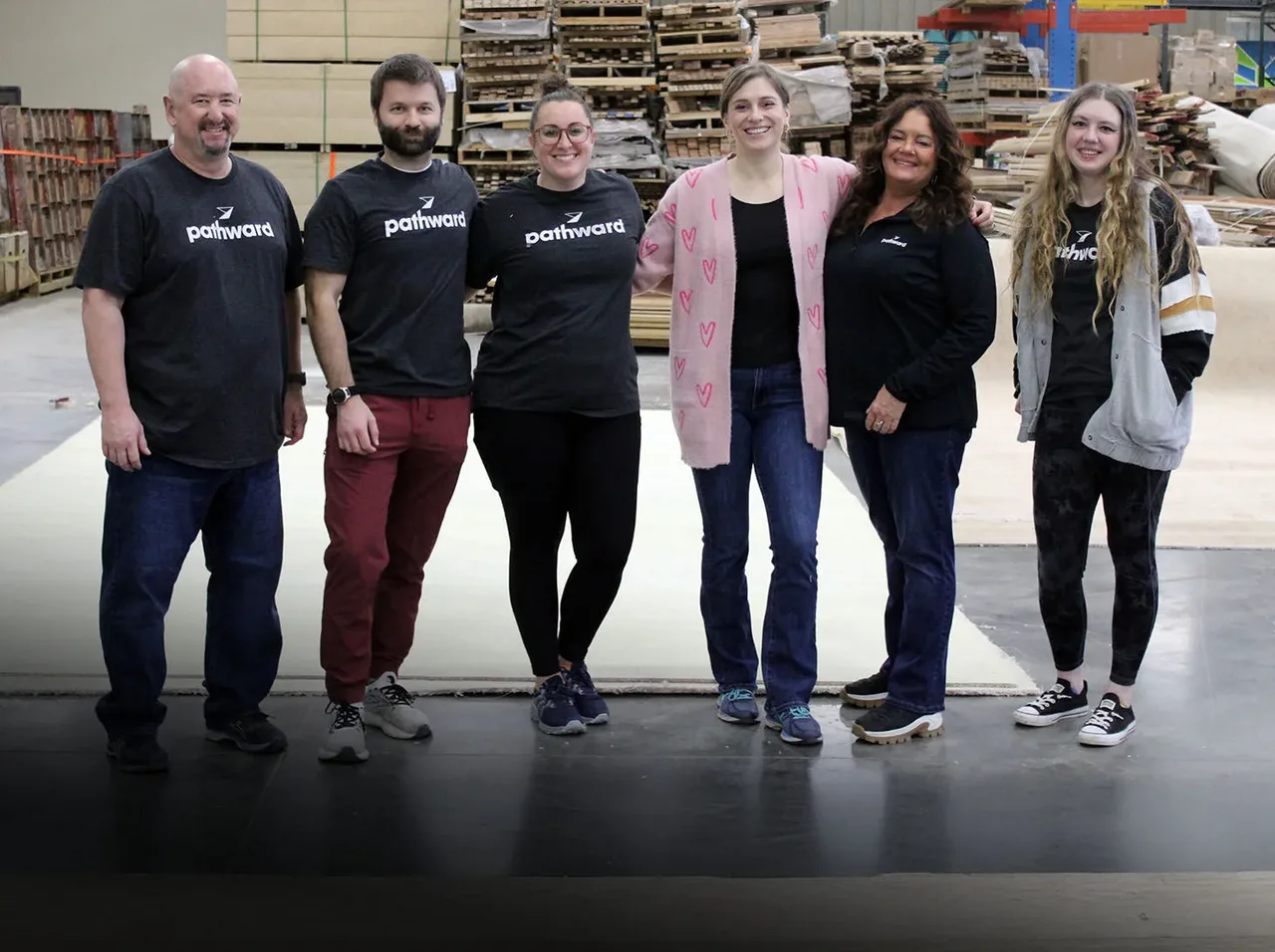 Six volunteers, most wearing Pathward shirts, standing together in a warehouse with stacked building materials.