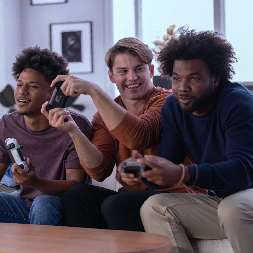 Three people sitting on a sofa playing video games with handheld controllers.