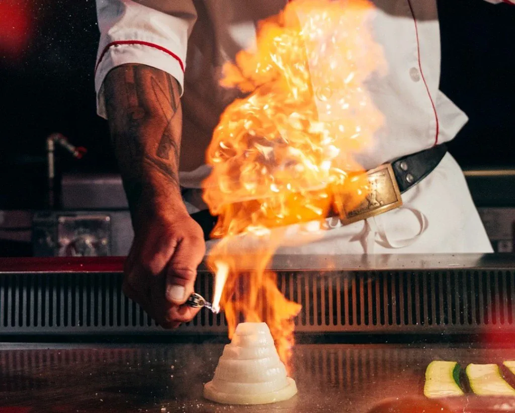 A Benihana chef lights an onion volcano on a teppanyaki grill.