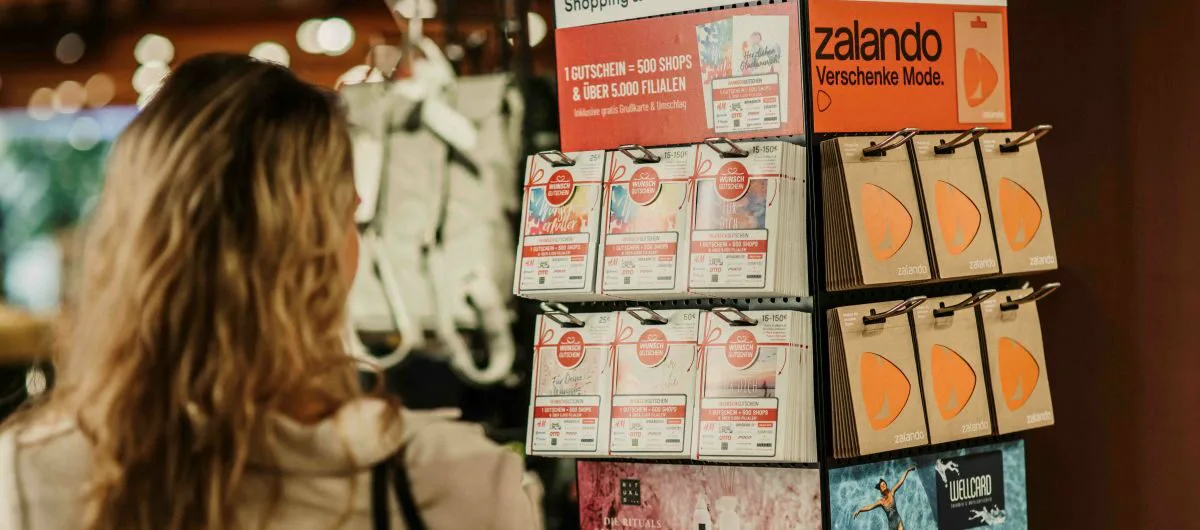 A shopper examines a rotating gift card display containing shopping and brand gift cards in a Thalia bookstore.