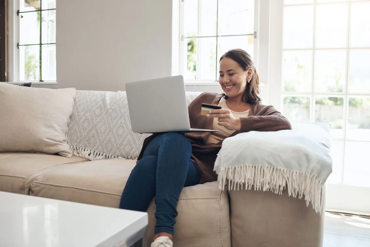 Woman holding a card and using a laptop at home