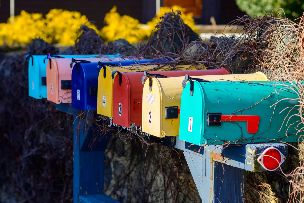 A row of colourful residential mailboxes beside a fence in the United States.
