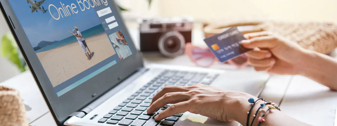 A person holding a payment card while using a laptop displaying a travel-booking website.