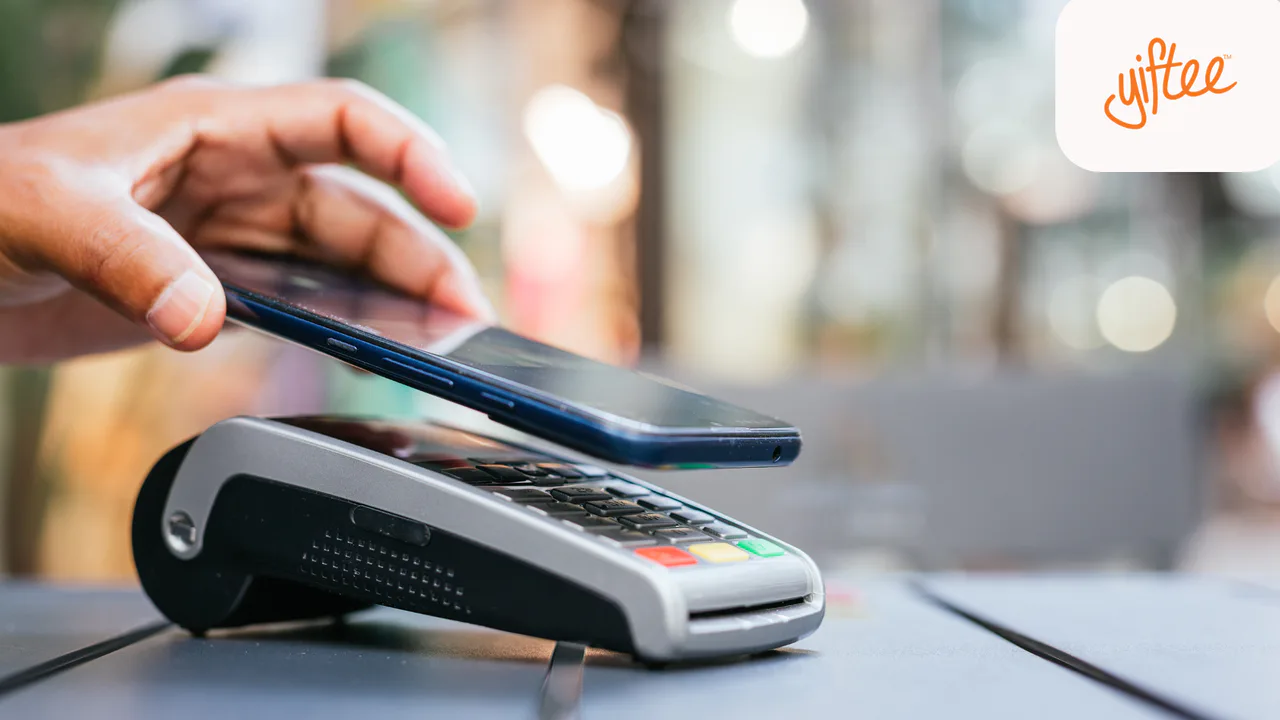 Yiftee promotional image of a hand holding a mobile phone above a contactless payment terminal.